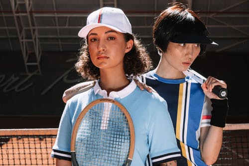 白色和蓝色的阿迪达斯乘员组脖子衬衫拿着橙色和白色网球拍的女人 · 免费素材图片