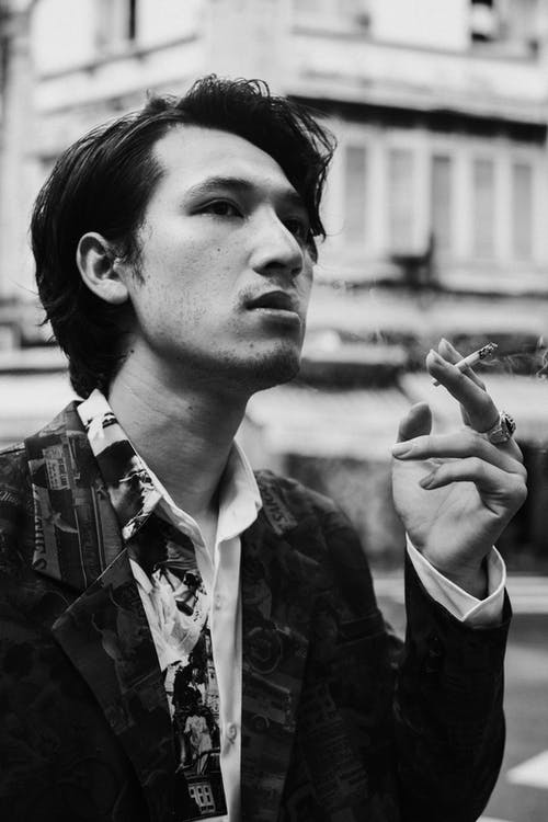 沉思的年轻民族男子在城市街道上吸烟 · 免费素材图片