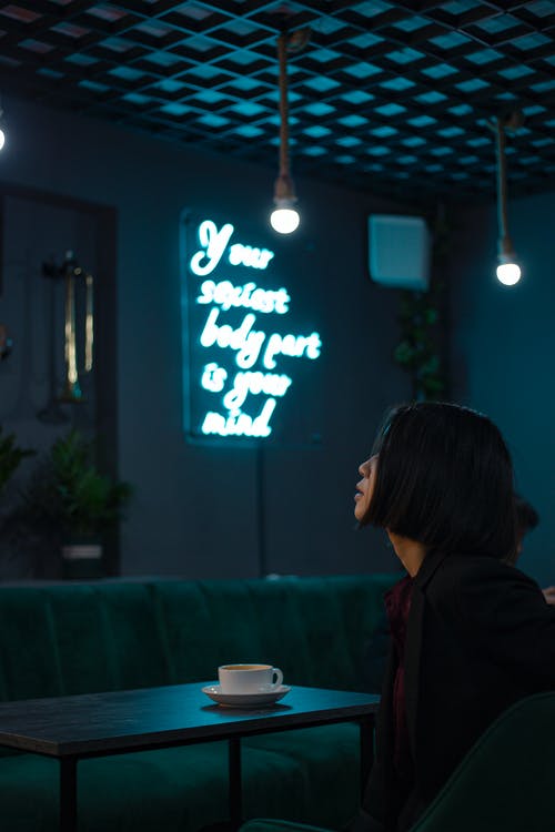 休息在咖啡馆与霓虹灯题字的年轻女子 · 免费素材图片
