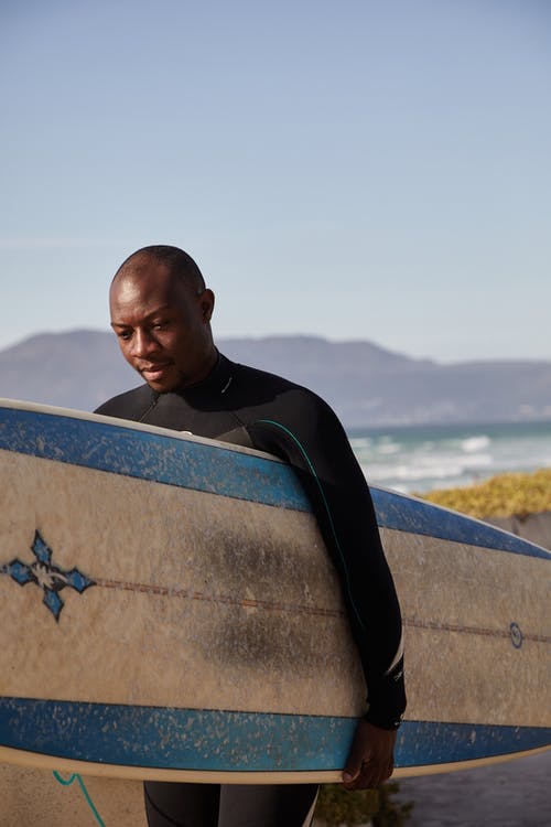 思考在海边的黑人冲浪者携带冲浪板 · 免费素材图片