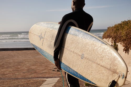 不可识别的黑人冲浪者在海边携带冲浪板 · 免费素材图片