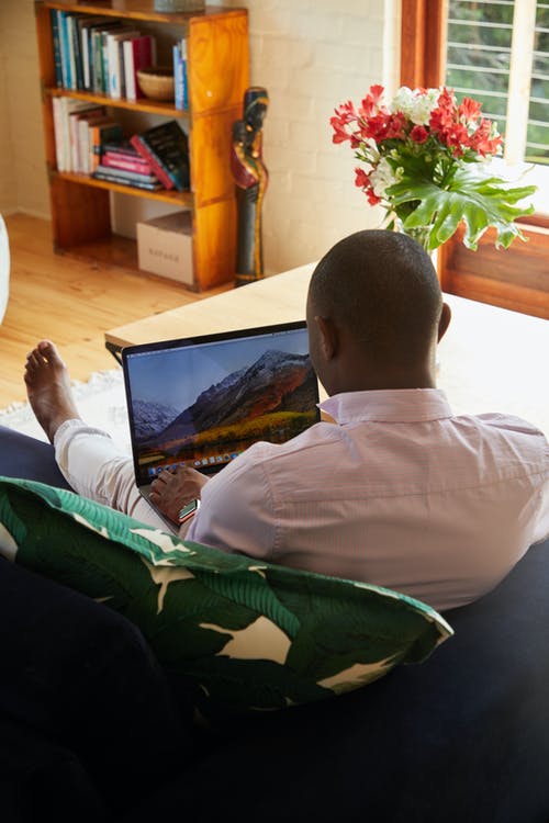 黑人在舒适的沙发上休息，浏览笔记本电脑 · 免费素材图片