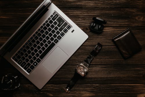 银色的macbook在棕色木制的桌子上的黑色圆形模拟手表旁边 · 免费素材图片