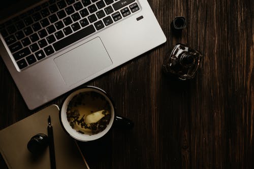 在黑色陶瓷杯旁边棕色木制的桌子上的银色macbook Pro · 免费素材图片