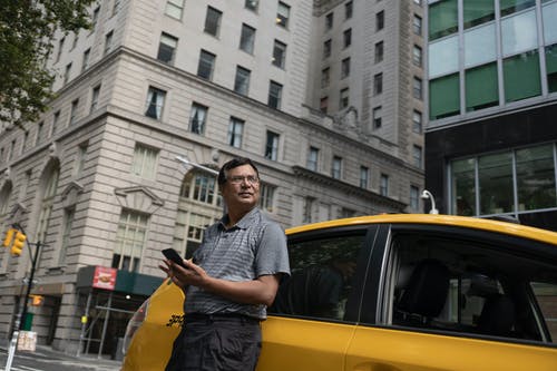 严重的民族男子，站在旁边的出租车与智能手机 · 免费素材图片