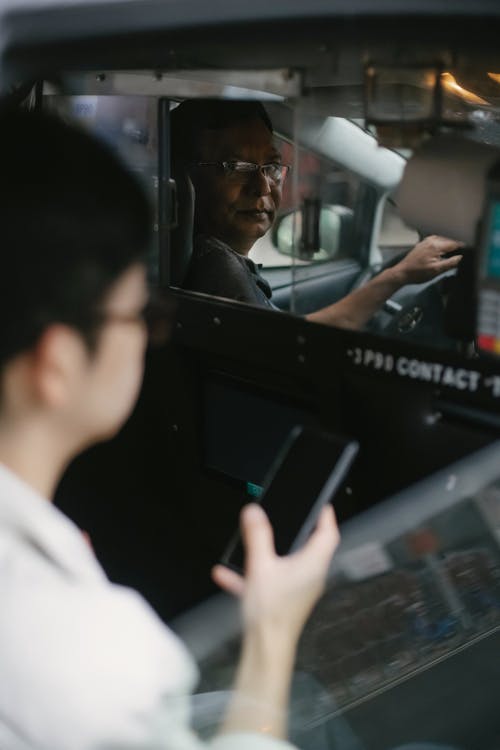 严重的出租车司机，透过窗户看乘客与智能手机 · 免费素材图片