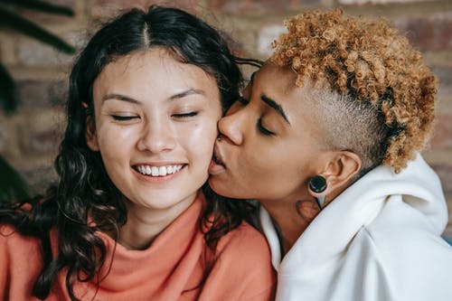 爱黑女人亲吻开朗的女友的脸颊 · 免费素材图片