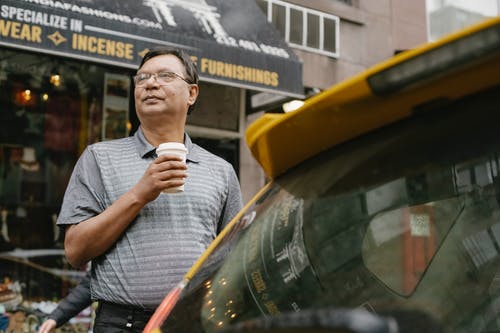 严重的族裔男子与汽车附近的咖啡 · 免费素材图片