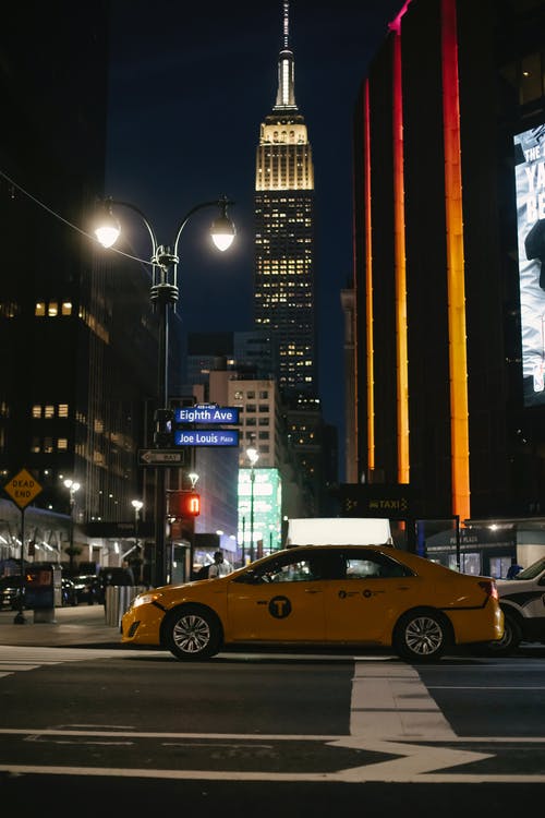 在晚上在现代摩天大楼附近的照明城市道路上的出租车 · 免费素材图片