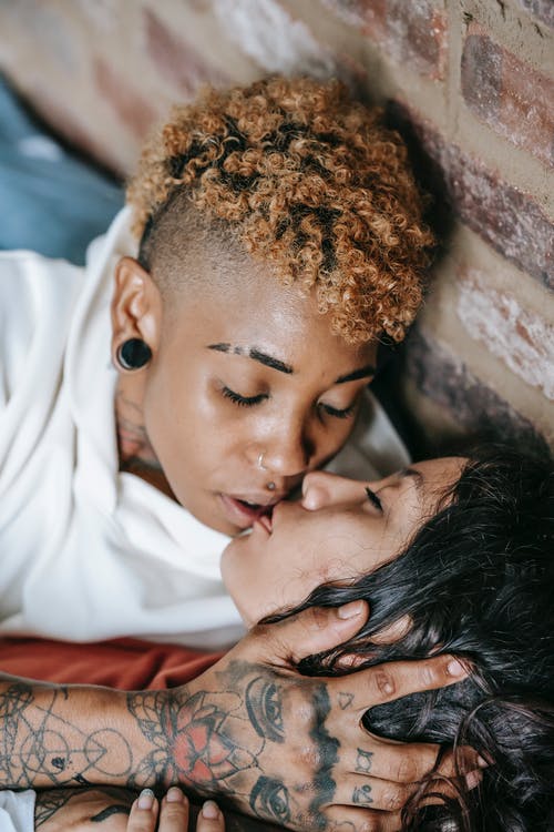 敏感的多种族女同性恋夫妇在砖墙附近接吻 · 免费素材图片