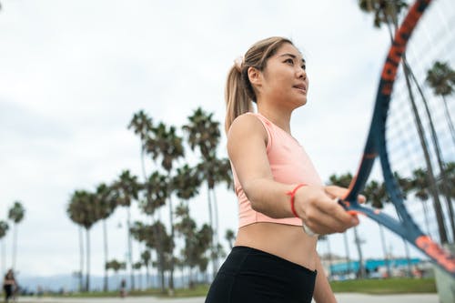 粉红色运动胸罩和黑色短裤拿着蓝色和黑色网球拍的女人 · 免费素材图片
