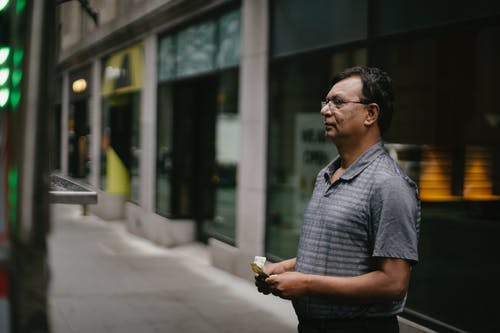 严重的族裔男子站在大街上的钱 · 免费素材图片