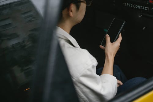 坐在后座上使用智能手机的出租车乘客的大角度 · 免费素材图片