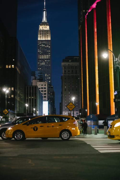 当代汽车在照明的摩天大楼附近的夜晚城市街道上骑 · 免费素材图片