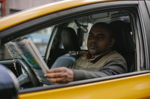 认真的族裔男性出租车司机阅读报纸 · 免费素材图片