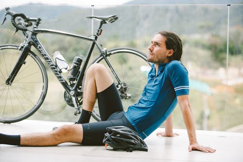 梦幻般的运动员在地板上的自行车附近休息 · 免费素材图片