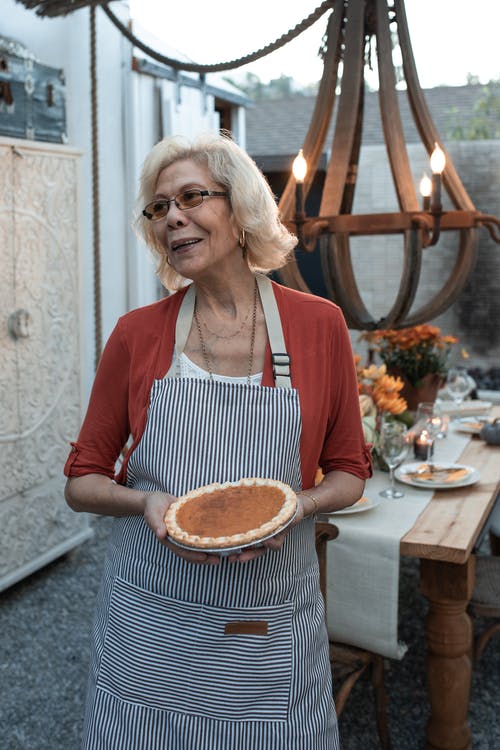 拿着棕色圆形蛋糕的红色和白色围裙的女人 · 免费素材图片