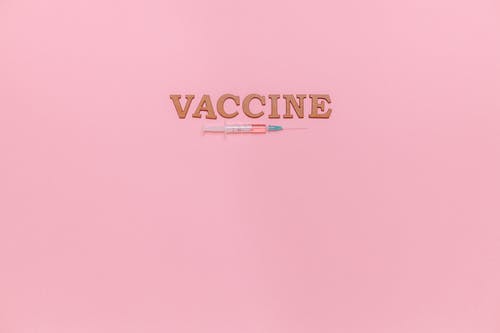 粉红色的背景上的注射器和疫苗文本 · 免费素材图片