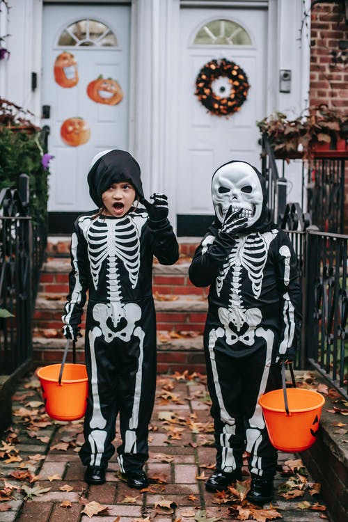 2个穿着黑色和白色骨架服装的男孩站在棕色的混凝土墙旁边 · 免费素材图片