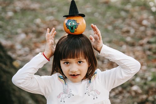 可爱的小女孩，用南瓜在头上保持平衡 · 免费素材图片