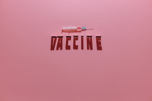 粉红色的背景上的注射器和疫苗刻字文本 · 免费素材图片