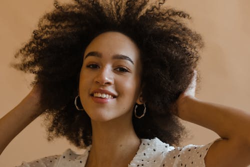性格开朗的年轻黑人女士抚摸非洲的头发，在工作室里微笑 · 免费素材图片