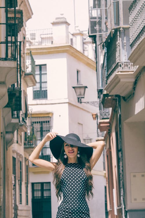 黑色和白色的波尔卡圆点裙，戴着黑帽子站在楼梯上的女人 · 免费素材图片