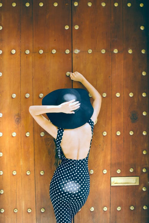 黑色和白色的波尔卡圆点裙，倚在棕色木墙上的女人 · 免费素材图片
