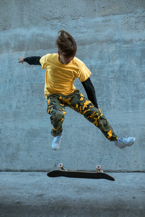 黄色衬衫和黑色的裤子，在黑色的滑板上跳跃的男孩 · 免费素材图片