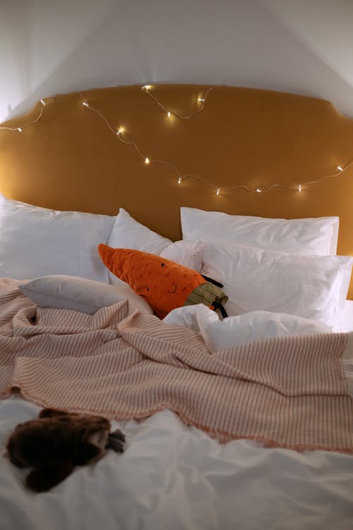 白色床上的橙色和白色扔枕头 · 免费素材图片