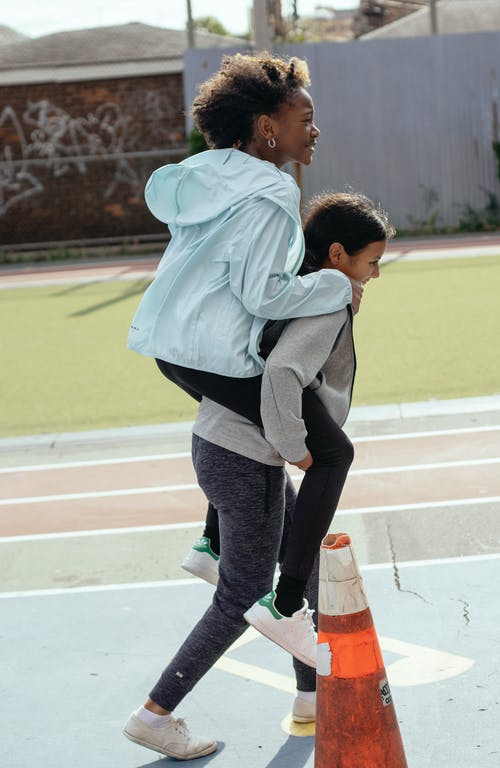 快乐的女孩背着同学背上同时在背景上玩 · 免费素材图片