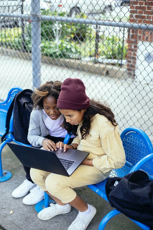 重点突出的多种族小学生在街头长椅上的笔记本电脑上浏览互联网 · 免费素材图片