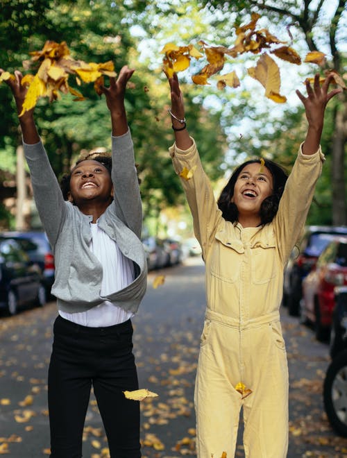 高兴的多民族女孩在大街上扔树叶 · 免费素材图片