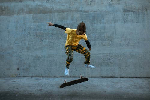 黄色的衬衫和绿色的裤子，在灰色的混凝土路上跳跃的女孩 · 免费素材图片