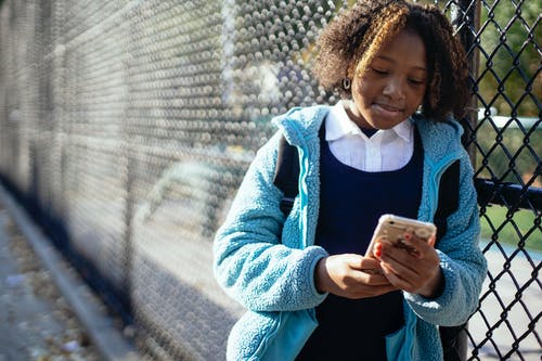 性格开朗的黑人女学生在大街上使用智能手机 · 免费素材图片