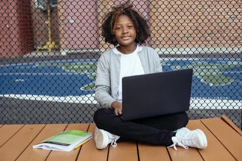 迷人的黑人女学生与笔记本电脑在大街上做作业 · 免费素材图片