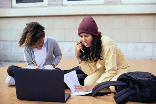 勤奋的多种族女学生做作业附近街上的笔记本电脑 · 免费素材图片