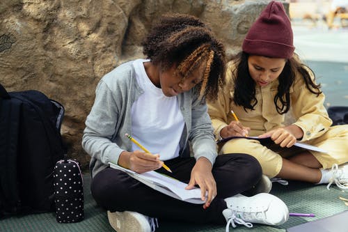 细心的多民族小学生在户外做作业时写在工作簿中 · 免费素材图片
