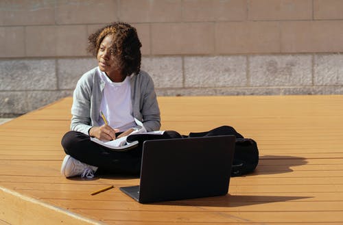 有工作簿和膝上型计算机的梦想的黑人女小学生学习在街道上 · 免费素材图片