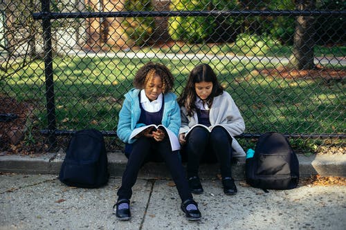 积极多样化的女学生在秋天公园的教科书中阅读主题 · 免费素材图片