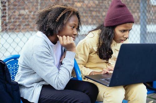 细心多样的女学生在街头的长椅上看笔记本电脑 · 免费素材图片