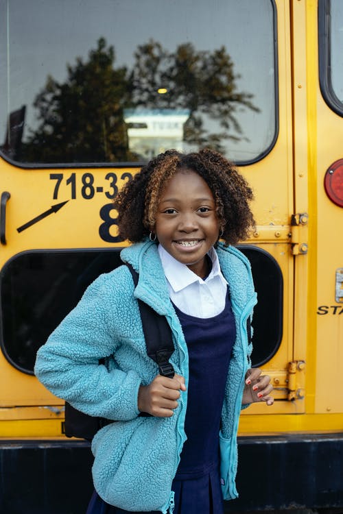 快乐的黑人女学生与背包站在校车附近 · 免费素材图片