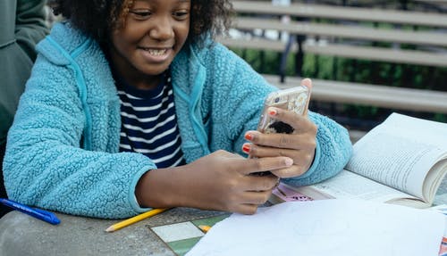 黑人女孩在作业期间浏览智能手机 · 免费素材图片