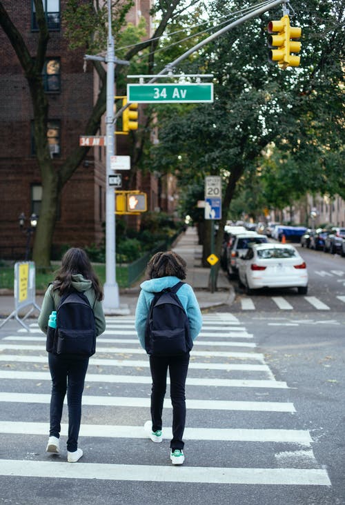 无法认出的女学生，背着背包穿越城市的道路 · 免费素材图片