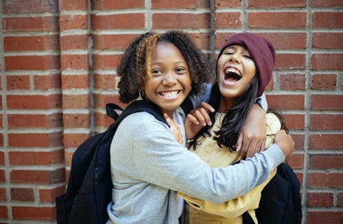 性格开朗的多样女生拥抱在砖墙附近 · 免费素材图片