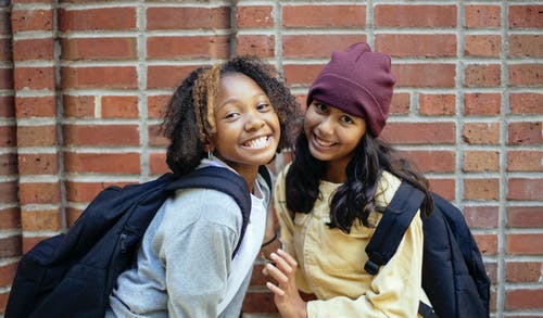 微笑与砖墙附近背囊的多样化的女学生 · 免费素材图片