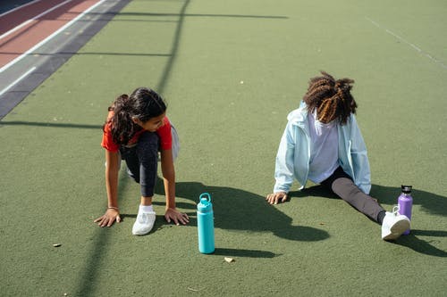 黑人女孩做拆分，而朋友在体育馆训练前伸展 · 免费素材图片