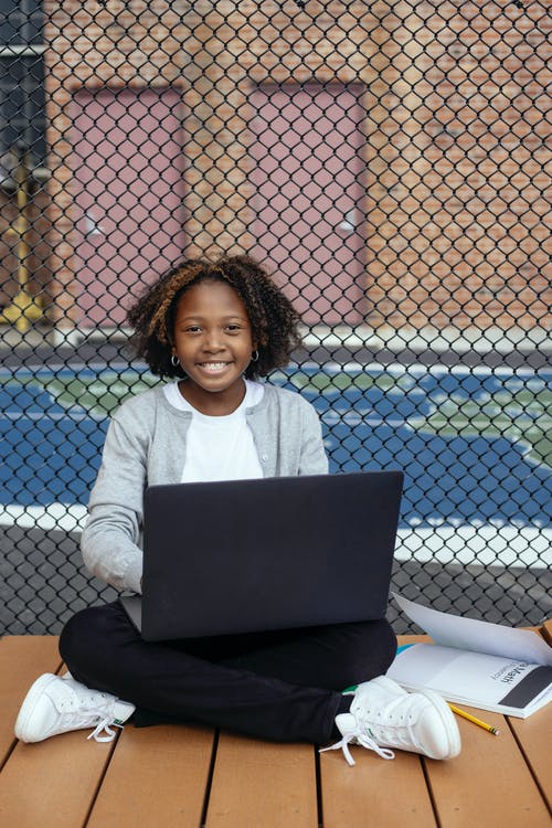 满意的黑人小学生用笔记本电脑学习网格栅栏附近 · 免费素材图片