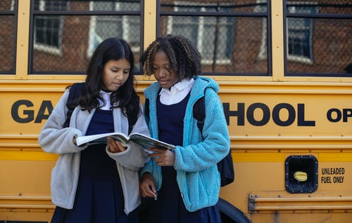多种族的女学生在城市公交车附近的工作簿 · 免费素材图片