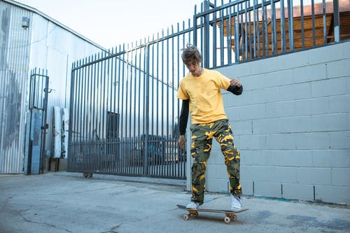 黄船员的脖子t恤和绿色迷彩裤站在灰色的水泥地板上的男人 · 免费素材图片